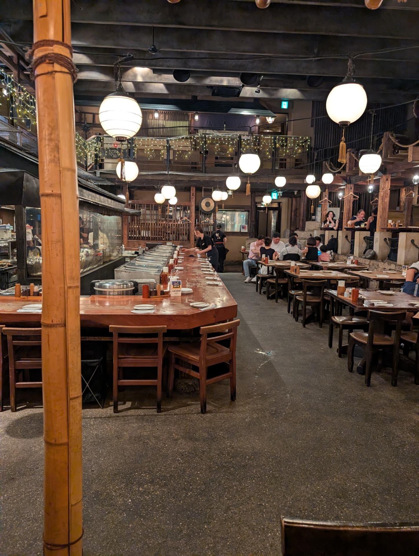 Stor izakaya med papperslyktor och långa bord